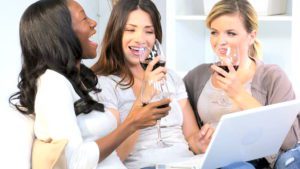 Three women are drinking wine and looking at a laptop.