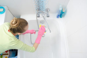 A woman in pink gloves cleaning the bathtub.