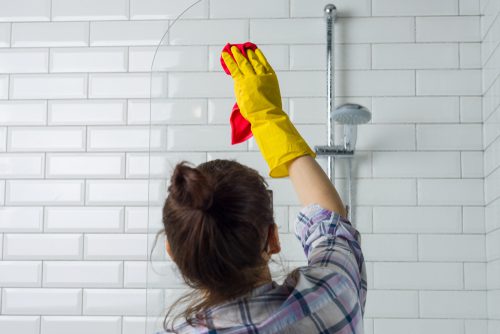 A woman in yellow gloves cleaning the shower.