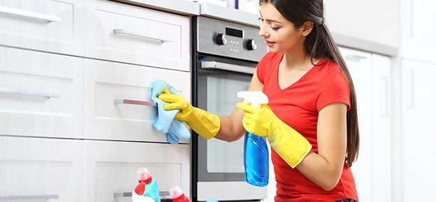 A woman in yellow gloves cleaning the kitchen.