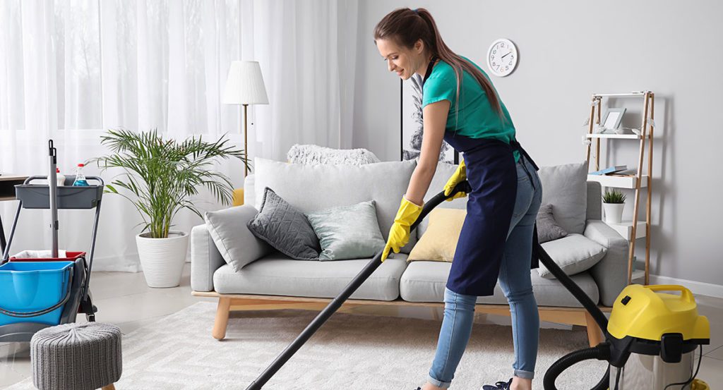 A woman in blue shirt holding a vacuum cleaner.