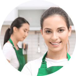 Two women in aprons are smiling for the camera.