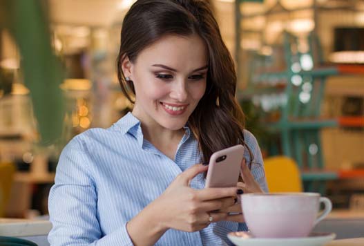 A woman is smiling while looking at her phone.