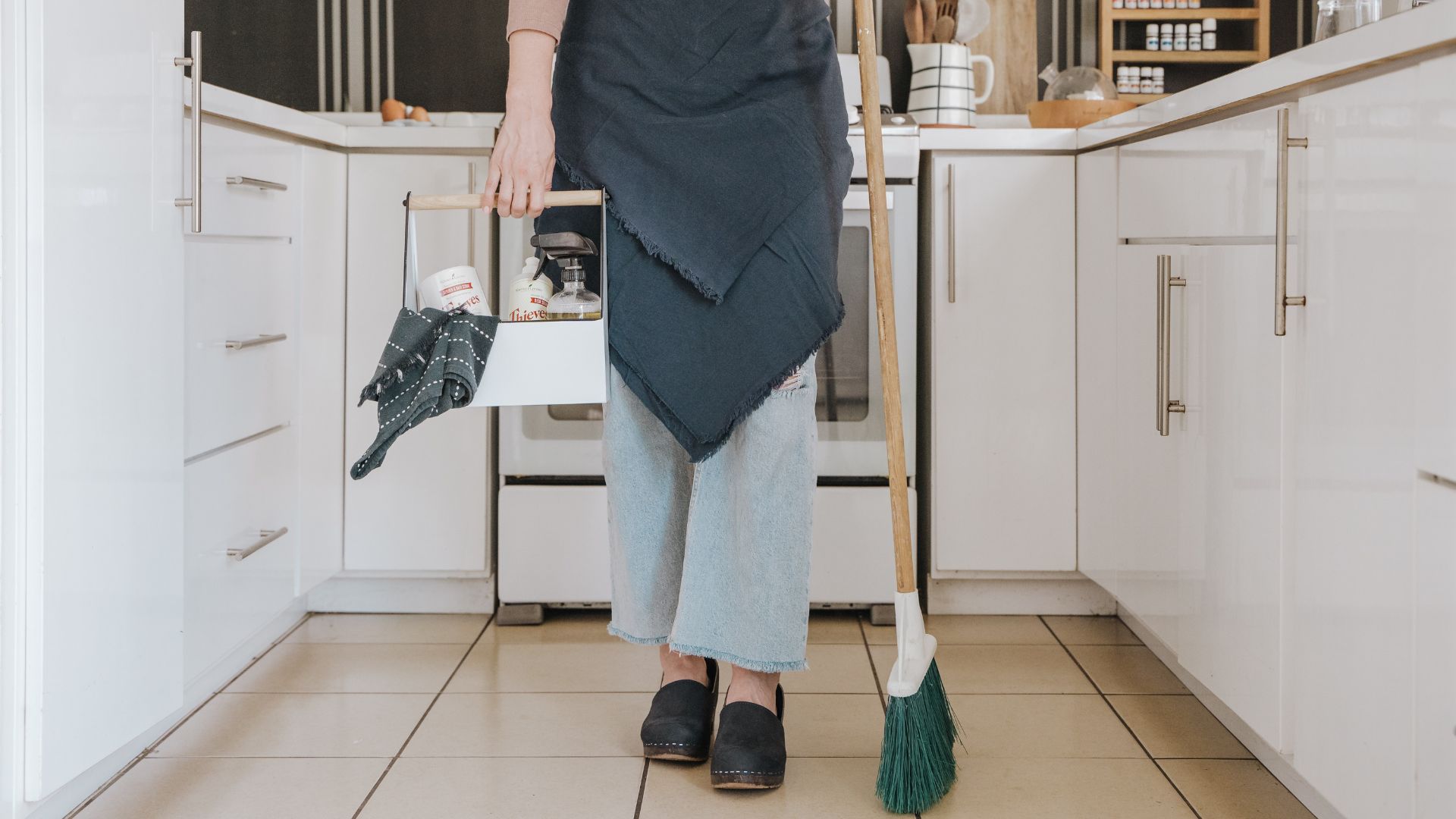 A person holding an umbrella and a mop in the kitchen.