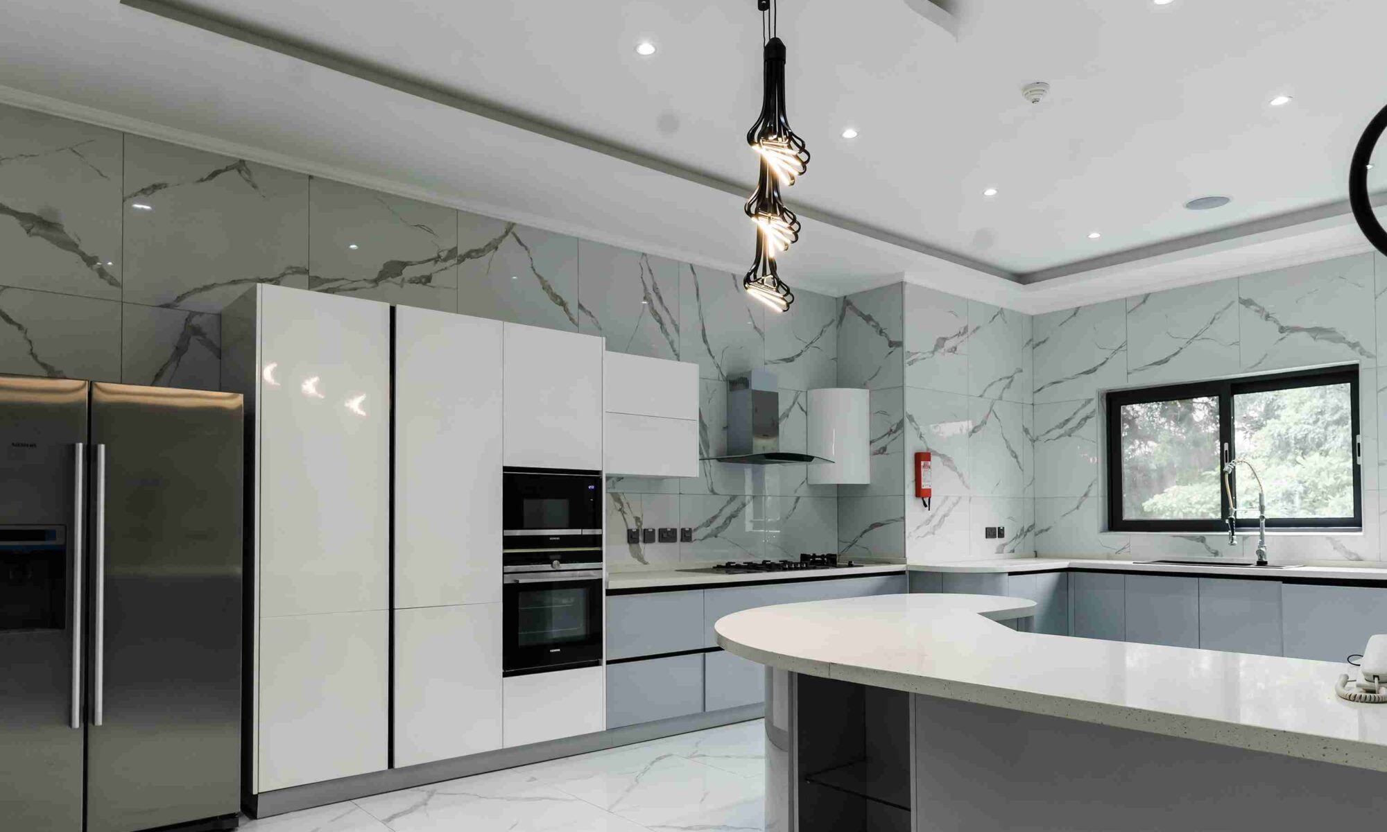 A kitchen with marble walls and floors, and white cabinets.